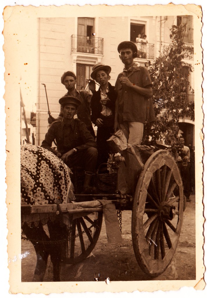 Quatre joves disfressats en un carro molt adornat, segurament en algun tipus de cavalcada. Són, d'esquerra a dreta, un desconegut, Vicente Vilara, Eladio i, ajupit, Vicente Pla.